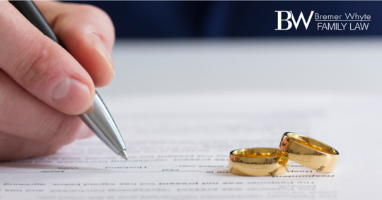 Image of person signing paperwork and two wedding rings nearby