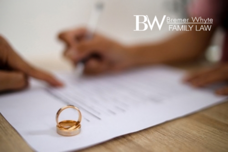Selective Focus of Wedding Rings Against Woman Hand Filing Divorce Papers or Premarital Agreement Prepared by Lawyer