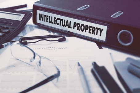 A black folder labeled "intellectual property" sits on a table with a clipboard, pens, a calculator, and glasses.